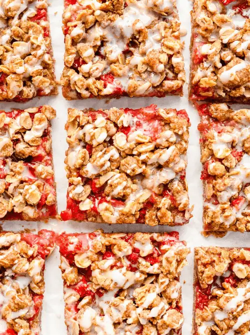 Overhead view of sliced strawberry oatmeal bars with fresh strawberry filling, oat crumble topping, and vanilla glaze arranged on parchment paper — an easy grab-and-go fresh strawberry brunch recipe.