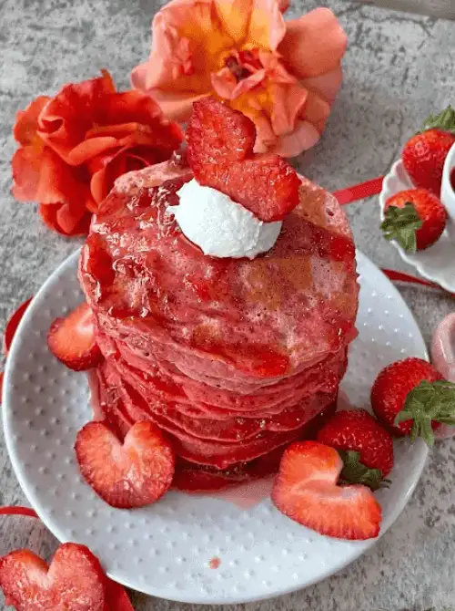 Tall stack of strawberry ombre pancakes in graduating shades of pink, topped with whipped cream and fresh sliced strawberries — a stunning fresh strawberry brunch recipe.