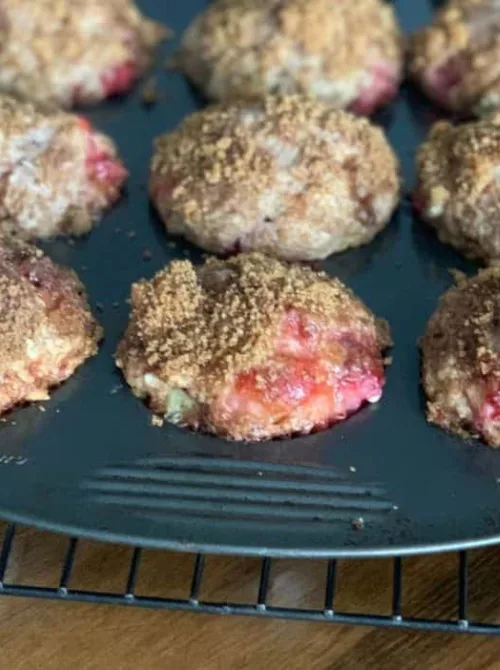 Freshly baked strawberry rhubarb muffins with cinnamon streusel topping cooling in a dark muffin tin — an easy make-ahead fresh strawberry brunch recipe.