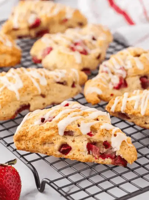 Flaky strawberry scones with vanilla glaze drizzled on top cooling on a wire rack with fresh strawberries — a make-ahead fresh strawberry brunch recipe.