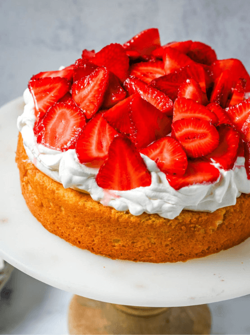 Single layer strawberry shortcake cake on a marble cake stand piled high with macerated fresh strawberries and whipped cream over a golden buttermilk sponge — a from-scratch homemade strawberry cake recipe with classic shortcake flavors in every slice
