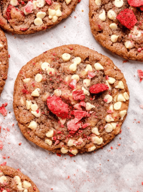 Close-up of a strawberry white chocolate chip cookie on parchment paper showing chunks of freeze-dried strawberries and white chocolate chips baked into a pink-tinted dough — one of the prettiest things to make with strawberries when you want a handheld summer treat.